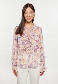 Blumenbluse aus weichem, leichtem Stoff mit lila und rosa Mustern, Rüschenausschnitt, einer Frontbindedetail und Knöpfen. Lange Ärmel mit Rüschensäumen.