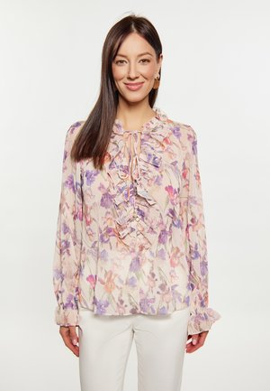 Blumenbluse aus weichem, leichtem Stoff mit lila und rosa Mustern, Rüschenausschnitt, einer Frontbindedetail und Knöpfen. Lange Ärmel mit Rüschensäumen.