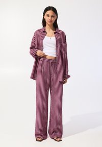 Set de pijama cu dungi purpurii, compus dintr-o bluză lejeră și pantaloni wide-leg. Fabricat dintr-un material ușor, cu o textură fină.