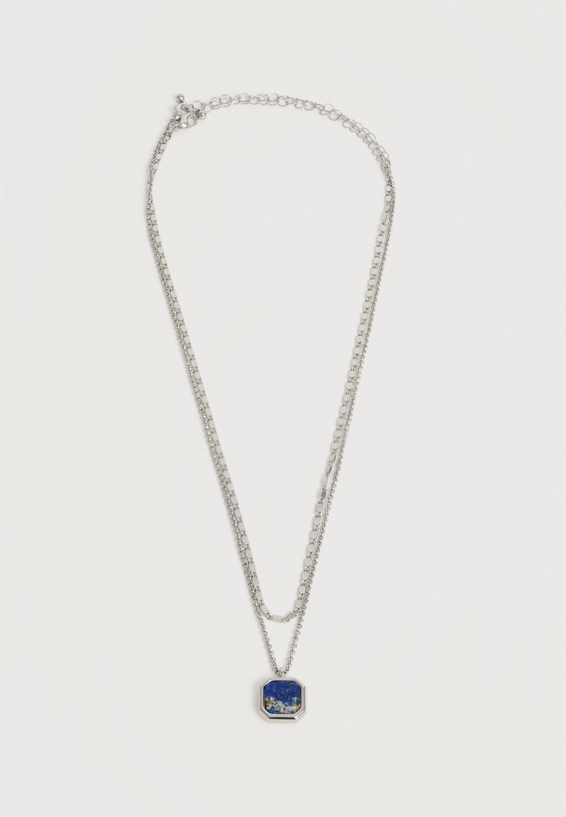 Ασημένιο διπλό κολιέ με τετράγωνο μπλε πέτρινο μενταγιόν που έχει λευκές και χρυσές βούλες σε ασημένιο πλαίσιο.