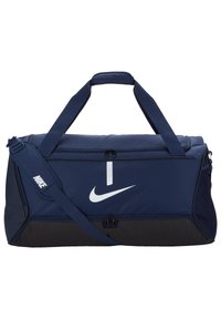 Marineblauwe sporttas van duurzaam materiaal, met een wit Nike-logo, dubbele handvatten bovenaan en een verstelbare schouderriem, voorzien van ritscompartimenten.