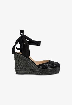 Espadrille noire à talon en forme de coin avec une base en jute tissé, un dessus en tissu texturé et des liens en satin assortis à la cheville. Présente un design de capuchon de orteils en perles.