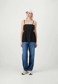 Črna brezrokavna majica s peplum dizajnom, v kombinaciji s svetlo modrimi ravnimi hlačami in belimi supergami. Model nosi belo kapo.