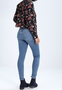 Černá krátká bunda s květinovým vzorem s červenými a bílými akcenty, doplněná úzkými modrými džíny do kotníků se mírně třepeným lemem a námořnickými botami.