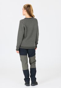 Grauer Pullover mit weißem Muster, Rundhalsausschnitt, kombiniert mit karierten Cargo-Hosen in Marineblau und Olivgrün. Mattes Material und taillierte Passform.
