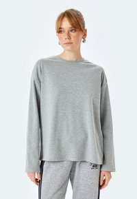 Graues Langarmshirt aus weichem Material mit lockerer Passform und rundem Ausschnitt, kombiniert mit grauen Hosen aus einem ähnlichen Stoff.