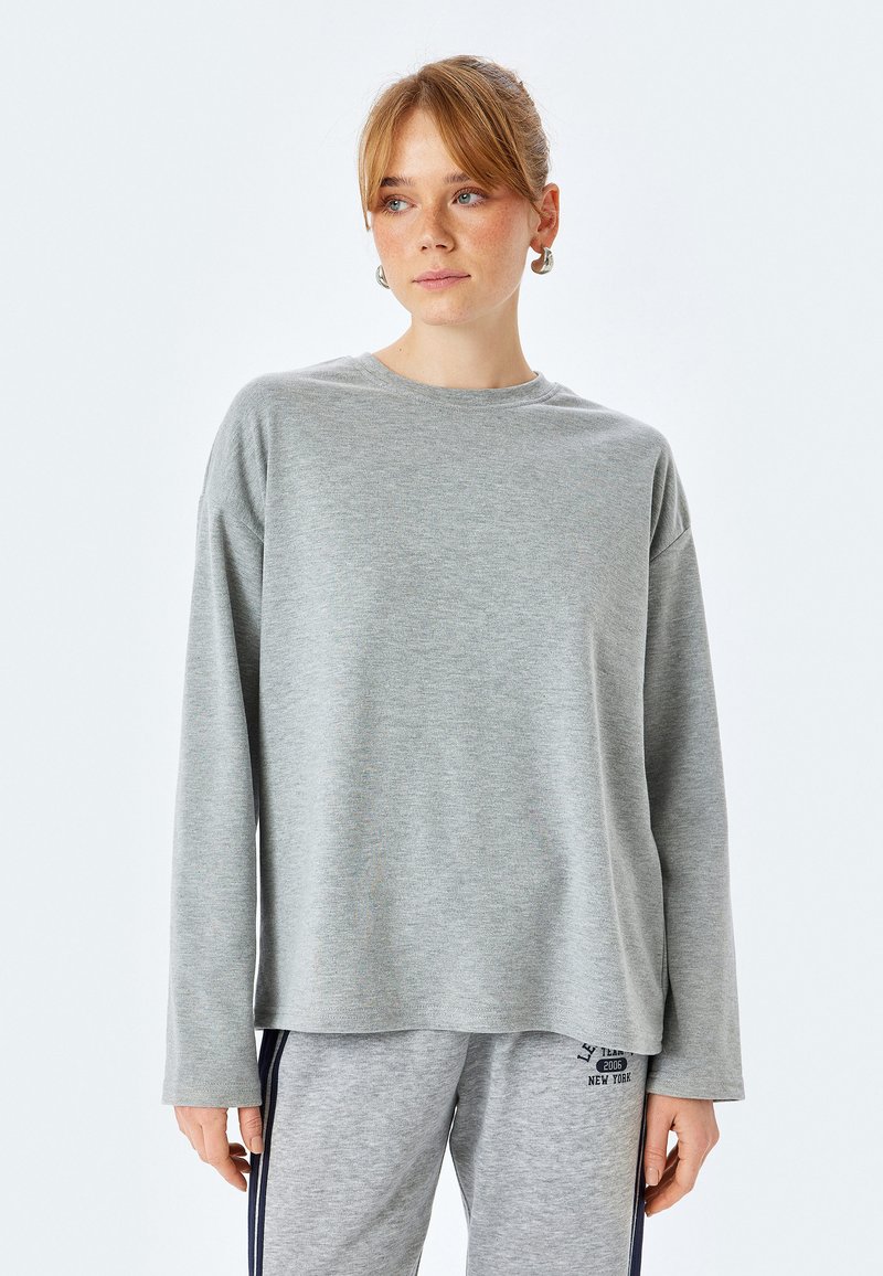 Graues Langarmshirt aus weichem Material mit lockerer Passform und rundem Ausschnitt, kombiniert mit grauen Hosen aus einem ähnlichen Stoff.