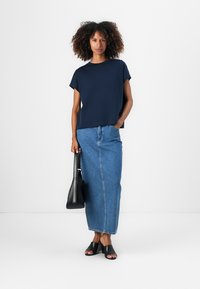 Marineblå kortermet topp parret med et langt denimskjørt, svarte slidesandaler og en svart håndveske. Enkelt, uformelt antrekk med avslappet passform.
