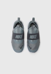 Nike vaikiški batai tamsiai pilko ir šviesiai pilko spalvų medžiagų. Yra ryški pilka dirželis su "NIKE" logotipu ir baltais guminiais padais.