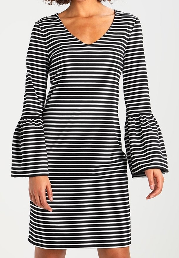 Mustavalkoinen raitapuku V-kaula-aukolla, jossa on pitkät kellohihat, tiukka vartalo ja pehmeä kangas.