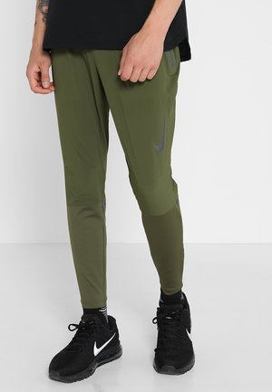 Pantalons de sport verts à coupe ajustée, fabriqués en matériau lisse ; dotés d'accents gris et de détails de ventilation. Portés avec des baskets noires.