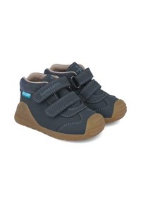 Zapatos de niño pequeños en azul marino con suelas de goma marrón, dobles correas de velcro y cuellos acolchados en los tobillos para mayor soporte y comodidad.