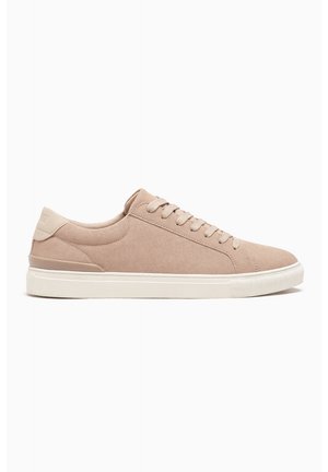 Beige ruskind lavtop-sneaker med beige snørebånd, polstret krave og hvid gummisål, set fra ydersiden mod en hvid baggrund.
