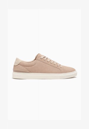 Zapatilla deportiva beige de ante con corte bajo, cordones beige, cuello acolchado y suela de goma blanca, vista desde el lado exterior sobre un fondo blanco.