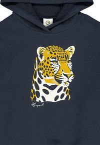 Musta huppari, jossa on leopardi grafiikka, joka korostaa keltaisia ja valkoisia karvakuviota erottuvilla mustilla täplillä ja yksityiskohtaisilla kasvonpiirteillä.