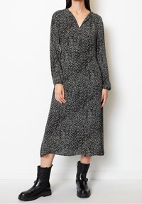 Schwarz-weiß gesprenkeltes langärmliges Kleid mit V-Ausschnitt und lockerer Passform, kombiniert mit klobigen schwarzen Stiefeln mit Reißverschluss und Schnallen-Detail.