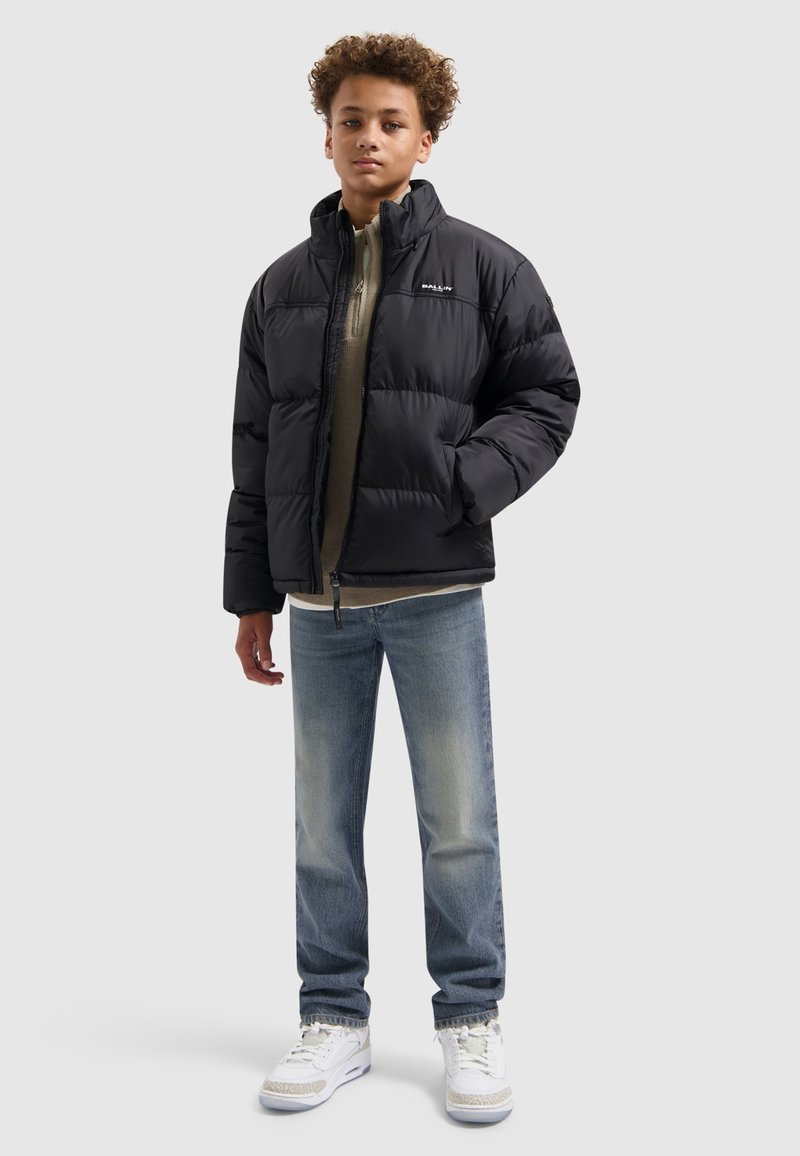 Zwarte pufferjack met een gekleed ontwerp, hoge kraag, vooraan met rits, gedragen over een beige top, gecombineerd met lichtblauwe jeans en witte sneakers.