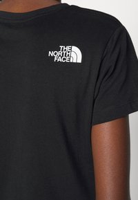 Svart bomulls-T-shirt med en vit logotyp av "The North Face" på övre ryggen, korta ärmar och en klassisk rundhalsdesign.