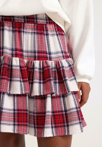 Rød og hvid ternet nederdel med flæser, lavet af tekstureret stof. Har en elastisk talje og skiftende tern i rød, hvid og marineblå.