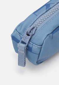 Blå tygpåse med en strukturerad yta, med en matchande dragkedja och en ögla som dragflik. Subtilt mönster integrerat i designen.