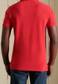 Polo rouge à manches courtes en coton, avec un col classique, un tissu texturé et des fentes latérales à l'ourlet pour un meilleur confort de mouvement.