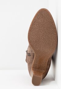 Stivale alla caviglia in suede marrone con suola in gomma testurizzata, dettaglio con cerniera laterale e punta rotonda. Impronta della taglia visibile sulla soletta interna.