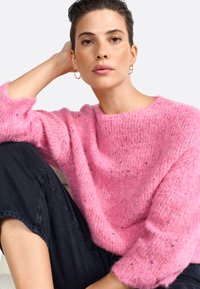 Maglione rosa lavorato a maglia con una vestibilità ampia e finitura testurizzata. Collo rotondo e maniche di lunghezza media. Abbinato a pantaloni in denim scuro.