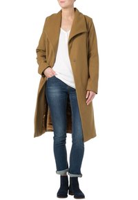 Abrigo largo marrón con un gran cuello, cierre de un solo botón y una textura suave, combinado con jeans azules y botas hasta el tobillo.