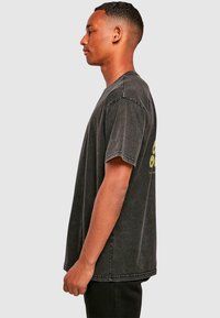 Dunkelgraues T-Shirt mit kurzen Ärmeln und lockerer Passform, mit verblasster Textur und gelb bedrucktem Grafikmotiv auf dem Rücken. Gerader Saum.