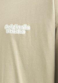 Beige sweatshirt lavet af blødt bomuld med rund hals; har ophøjet hvid broderi med teksten "Originals Studio" på brystet.