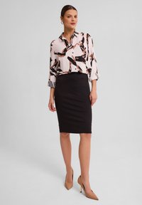 Bluzka z różowym tłem i abstrakcyjnymi czarnymi oraz brzoskwiniowymi wzorami; zestawiona z czarną spódnicą ołówkową i cielistymi szpilkami.