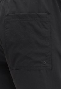 Κοντινή λήψη μαύρου υφασμάτινου παντελονιού που δείχνει μια ορθογώνια πίσω τσέπη με ορατή ραφή και μια μικρή κεντημένη λεπτομέρεια τρύπας.