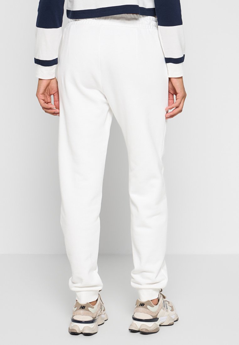 Weiße Sweatpants mit elastischem Bund, schmal zulaufenden Bündchen und glatter Textur, kombiniert mit beigen Sneakers. Keine sichtbaren Muster oder Logos.