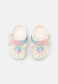 Weiße Clogs mit einem Regenbogenverlauf-Riemen, einem Einhornhorn und -ohren sowie runden Belüftungslöchern. Weiches, leichtes Material.