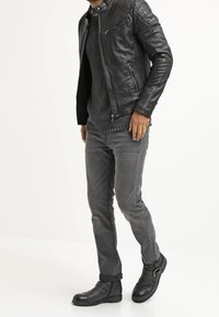 Svart läderjacka med quiltade axelpartier, grå stickad tröja, grå jeans och svarta ankelboots med spänne.