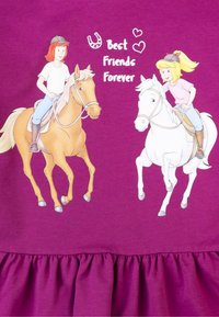 Lila Baumwollkleid mit Rüschensaum, das zwei Mädchen auf Pferden zeigt, mit dem Text "Beste Freunde für immer" und einer Hufeisengrafik.