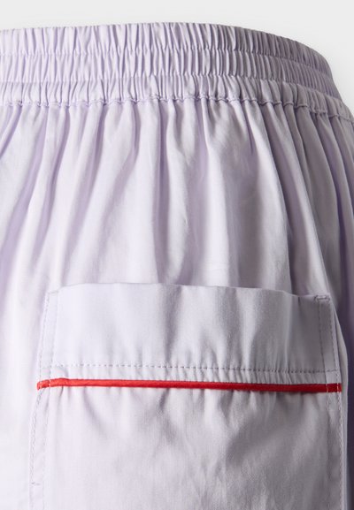 Ελαστική μέση σε ανοιχτό μωβ χρώμα με σορτς που έχουν μια μεγάλη πίσω τσέπη με οριζόντια κόκκινη διακοσμητική λεπτομέρεια.