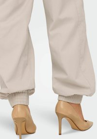 Bež jogger hlače s elastičnim manžetama uparenih s nude štiklama s otpointed prstom i elegantnim završetkom.