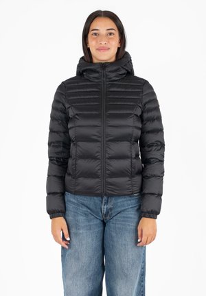 Zwarte, pufferjack met rits en capuchon, met horizontale stiknaden en elastische manchetten. Draagt over lichtblauwe, losse jeans.