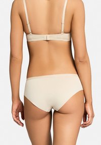 Beżowy komplet biustonosza i majtek, gładki materiał, regulowane ramiączka, bezszwowy design oraz minimalistyczny krój zapewniający komfort i dopasowanie.