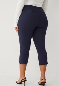 Pantaloni capri blu navy con una vestibilità aderente, dotati di una singola tasca posteriore. Realizzati in un tessuto morbido e elasticizzato con un orlo pulito.