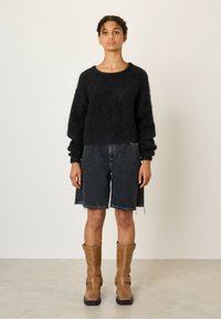 Juodas pūkuotas megztinis su apvaliu kaklu, derinamas su tamsiais džinsiniais šortais su suplėšytais galiukais ir rudiemedžiu iki kelių batais.