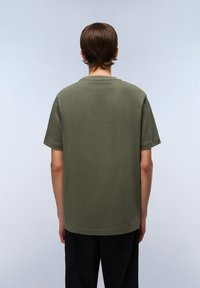 Olivengrøn kortærmet t-shirt med afslappet pasform, rund halsudskæring og glat bomuldsstruktur, parret med sorte bukser.