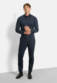 Navyblauwe button-up shirt met witte stippen, lange mouwen. Gecombineerd met navy chinos en zwarte schoenen. Eenvoudig ontwerp, getailleerde pasvorm.