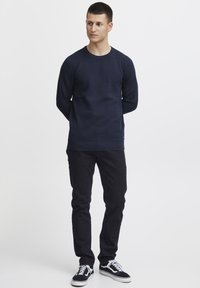 Tumed tekstuuriga pikkade varrukatega särk ümmarguse kaelusega, kombineeritud mustade teksade ja musta-valgete madalate tossudega.