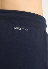 Marinblå träningsshorts gjorda av mjukt tyg, med en ribbad midja och texten "ONLY PLAY" i silver.