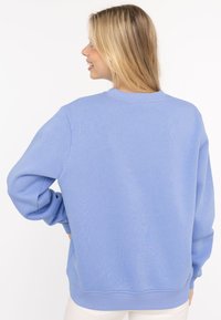 Jasnoniebieska bluza z bawełnianej tkaniny mieszanej, z długimi rękawami, okrągłym dekoltem oraz ściągaczami na rękawach i u dołu. Gładka tekstura.