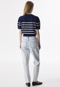 Navy gestreept T-shirt met korte mouwen en witte strepen, gecombineerd met lichtblauwe denimjeans. De outfit heeft een relaxte pasvorm en minimale details.