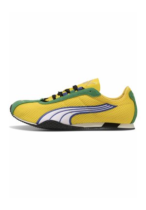 Gele mesh sneaker met groene suède afwerking, zwarte veters en wit Puma-logo met blauwe omlijning aan de zijkant.
