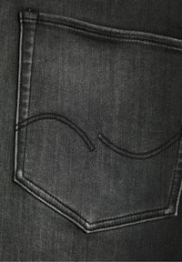 Svarta denimjeansfickor med krökta sömmar, har en strukturerad yta och en distinkt, vinkelränt fickform.